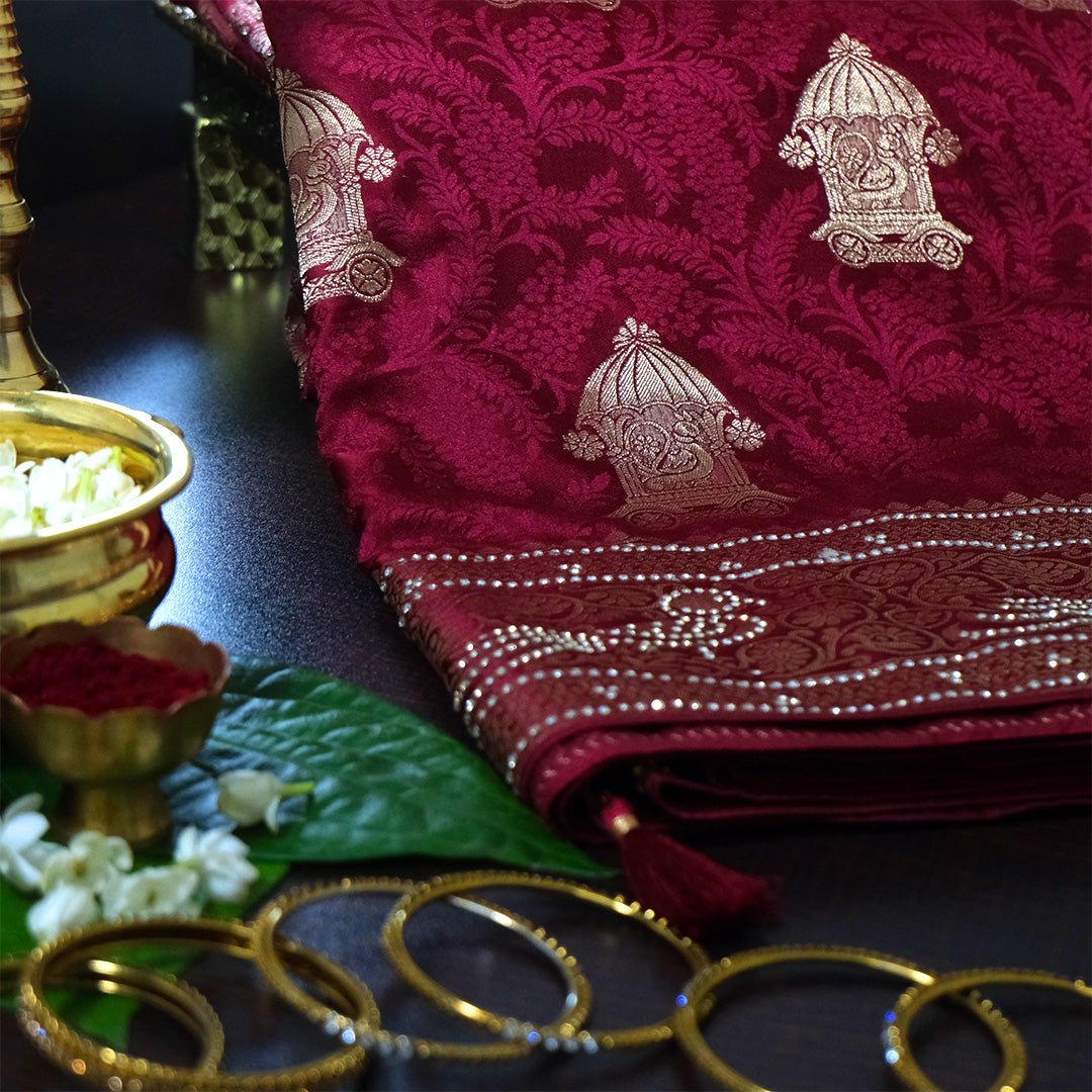 Royal Ratha Banarasi silk in deep maroon red shade, highlighted with rich golden zari motifs and an ornate golden border.